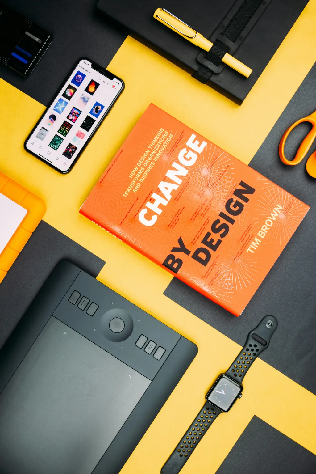 Mesa de trabalho com livro "Change By Design de Tim Brown" sobre mudança pelo design e vários objetos com atenção particular ao Branding